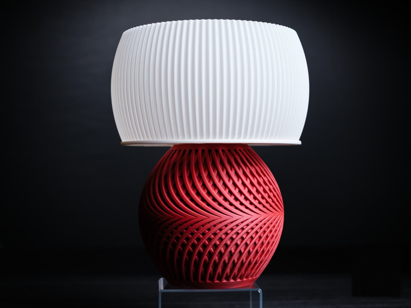 La lampe Drift, abat-jour plissé blanc sur une base tressée rouge foncé.